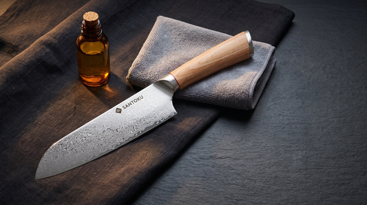 Santoku Knives Damascus santoku on dark linen beside a microfibre cloth and a bottle of food-safe camellia oil